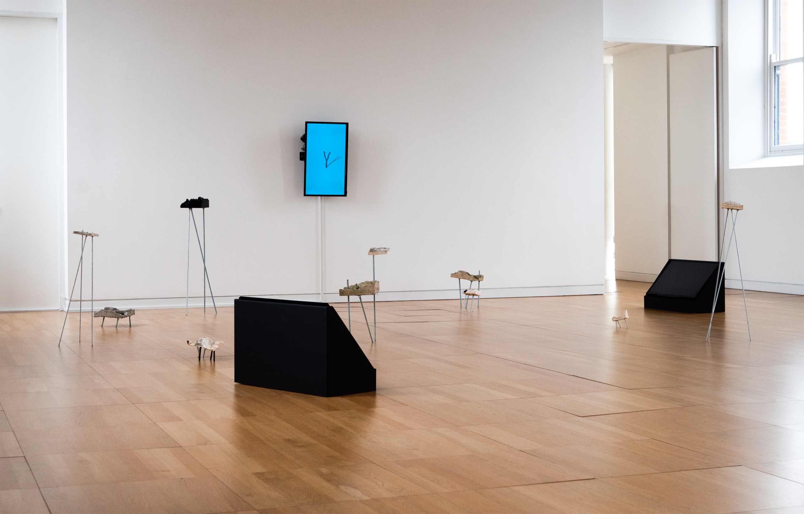 Art on legs on the floor with a screen on the wall at the exhibition Athrú at Luan Gallery