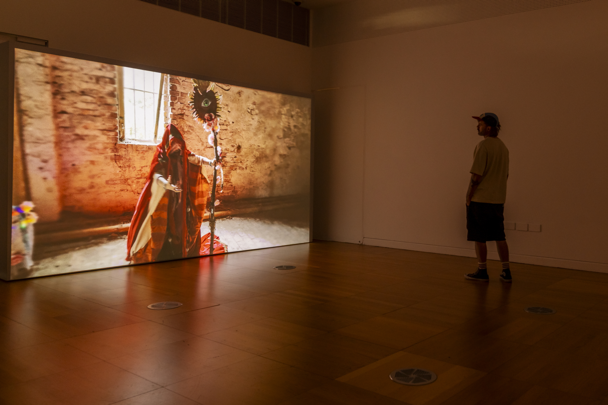 Lighted art or screen on wall in a dark room with one viewer at the exhibition Soft Surge at Luan Gallery