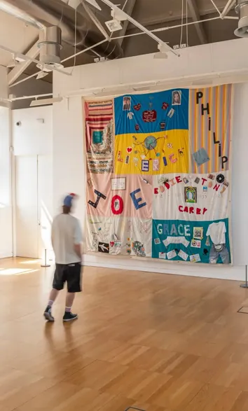 Big patchwork art with names on a white wall with a viewer at Luan Gallery